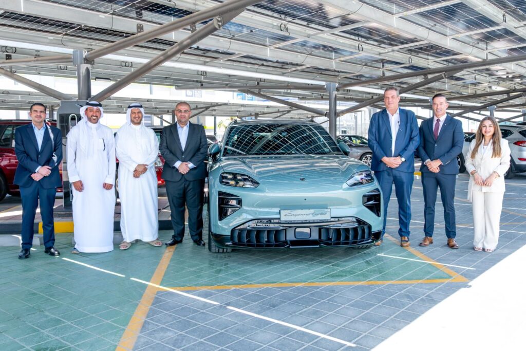 Kanoo Real Estate and Behbehani Brothers representatives beside a Porsche electric vehicle at Sitra Service Station, Bahrain.