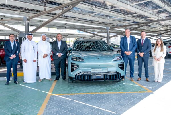 Kanoo Real Estate and Behbehani Brothers representatives beside a Porsche electric vehicle at Sitra Service Station, Bahrain.