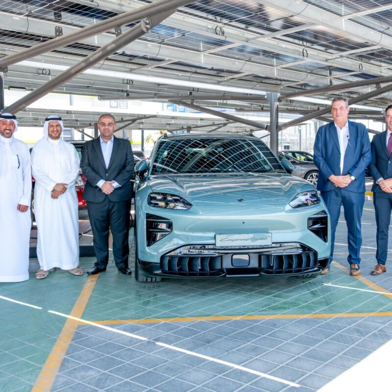 Kanoo Real Estate and Behbehani Brothers representatives beside a Porsche electric vehicle at Sitra Service Station, Bahrain.
