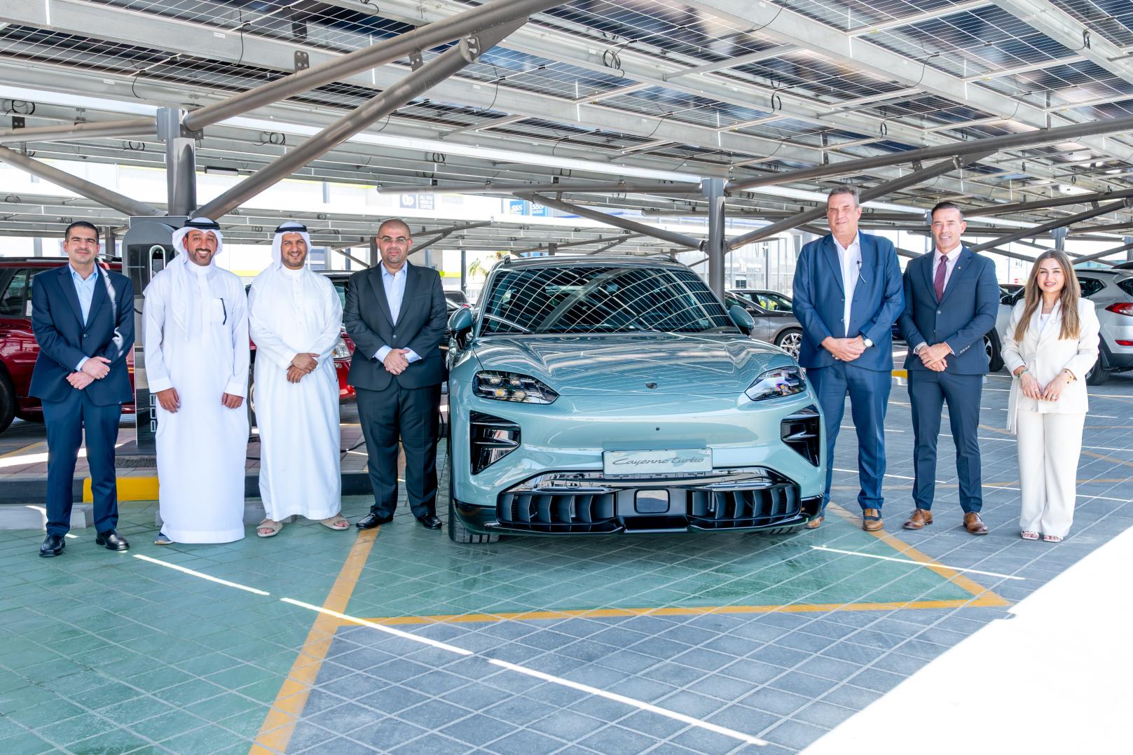 Kanoo Real Estate and Behbehani Brothers representatives beside a Porsche electric vehicle at Sitra Service Station, Bahrain.